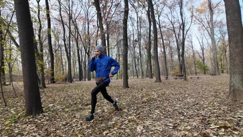 Athletic man in blue jacket and gray beanie runs quickly towards the camera in Stock Footage 316844029