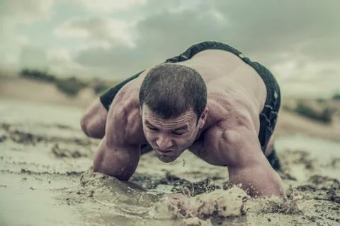 Athletic man crawling in wet muddy puddle Stock Photos