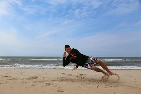 Athletic man diagonal lean pose on beach, tilted posture, action movement Foto stock