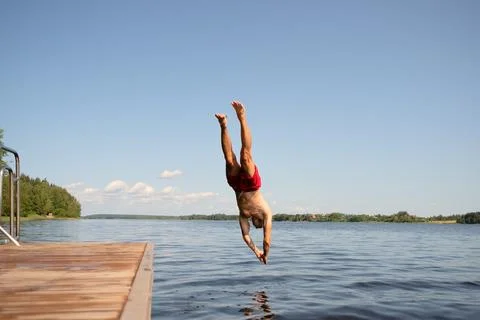 Athletic man diving headfirst from a pier into the lake. Summer day, strong Stock-Fotos