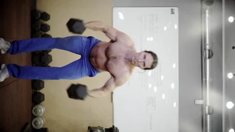 Athletic man does exercises with dumbbells, trains shoulders, vertical video Video stock 126673091