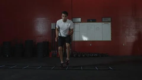 Athletic man does side step ladder exercise in gym Stock Photos
