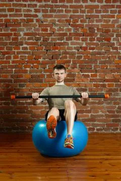 Athletic man doing balancing exercises over the gym ball with gymnastic stick Foto stock