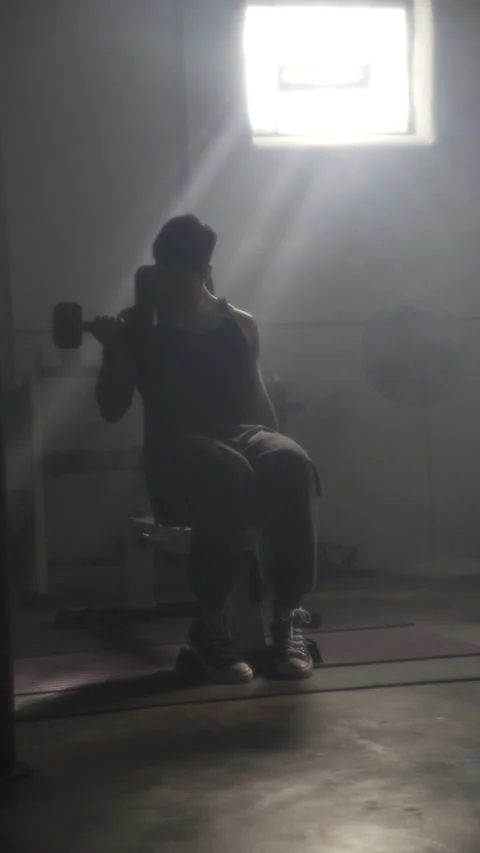 Athletic man doing biceps curls with dumbbells while sitting on a bench in a Stock Footage 344166297