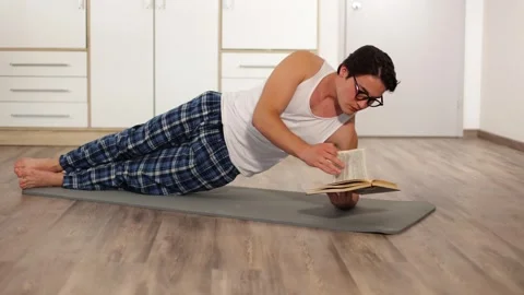 Athletic man is doing exercises standing in side elbow plank at home read book Vidéo 253827270