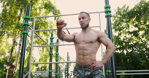 Athletic man doing exercises for triceps with resistance band outdoors on warm 스톡 동영상 157453033