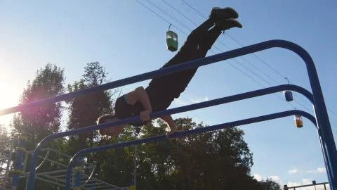 Athletic man doing gymnastics elements on bar in city park. Male sportsman Fotos Stock