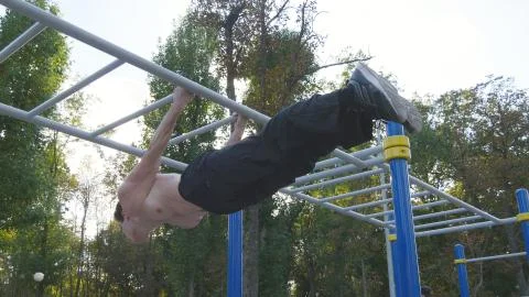 Athletic man doing gymnastics elements on horizontal bar in city park. Male Fotos Stock