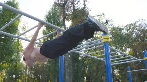 Athletic man doing gymnastics elements on horizontal bar in city park. Male Fotos Stock