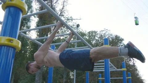 Athletic man doing gymnastics elements on horizontal bar in city park. Male Fotos Stock