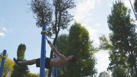 Athletic man doing gymnastics elements on horizontal bar in city park. Male Fotos Stock