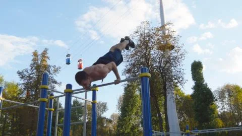 Athletic man doing gymnastics elements on horizontal bar in city park. Male Fotos Stock