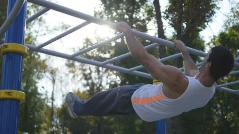 Athletic man doing lifting body on horizontal bar in city park. Male sportsman Stock Photos
