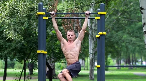 Athletic man doing lifting legs on horizontal bar in City Park. Athletic man Vidéo 66420757