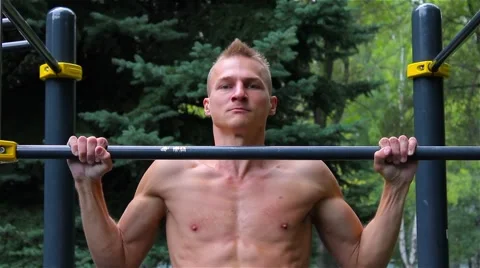 Athletic man doing pull ups on horizontal bar in City Park. front view. Workout Stock Footage 66420716