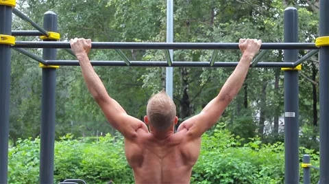 Athletic man doing pull ups on horizontal bar in City Park. rear view. Workout Stock Footage 66420725
