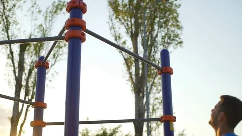 Athletic man doing pull ups on horizontal bar park sunrise workout slow motion Stock Footage 76779979