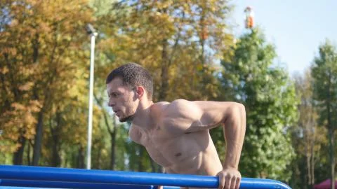 Athletic man doing push ups on parallel bars at sports ground in city park Stock-Fotos