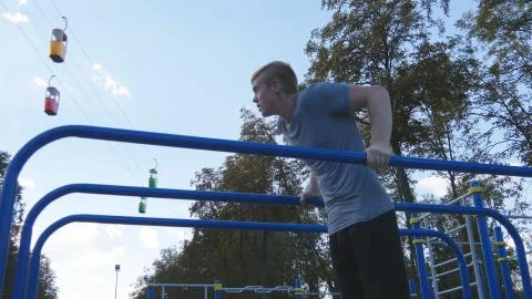 Athletic man doing push ups on parallel bars at sports ground in city park 写真素材