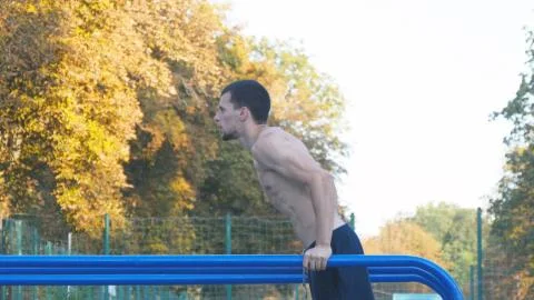 Athletic man doing push ups on parallel bars at sports ground in city park Stock Photos