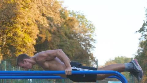 Athletic man doing push ups on parallel bars at sports ground in city park 스톡 사진