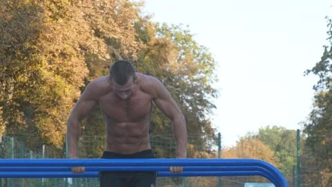 Athletic man doing push ups on parallel bars at sports ground in city park 스톡 사진
