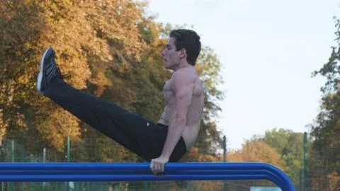Athletic man doing push ups on parallel bars at sports ground in city park Stock Photos