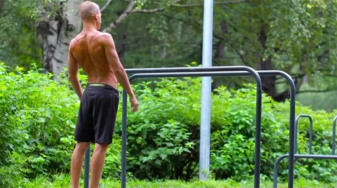 Athletic man doing warm-up before exercise on bars in City Park under summer Stock Footage 66420642