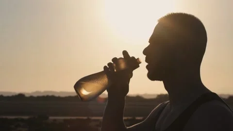 Athletic man drinking water after workout outdoors, backlit silhouette shot Stock Footage 132166217