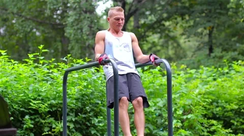 Athletic man exercise the abdominals on bars in City Park under summer trees for Video stock 66420639
