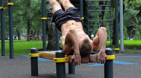 Athletic man exercise the abdominals on bench in City Park under summer trees Stock Footage 66420745
