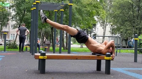 Athletic man exercise the abdominals on bench in City Park under summer trees 動画素材 66420749