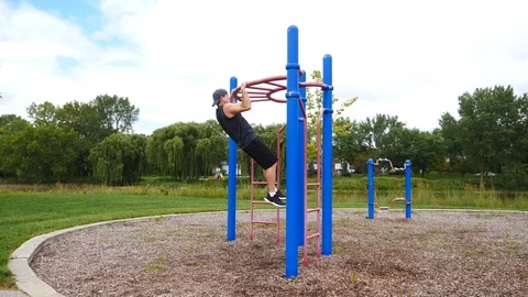 Athletic man exercising doing pull ups in a park on a summer day, 4k, 60fps. Stock Footage 115900527