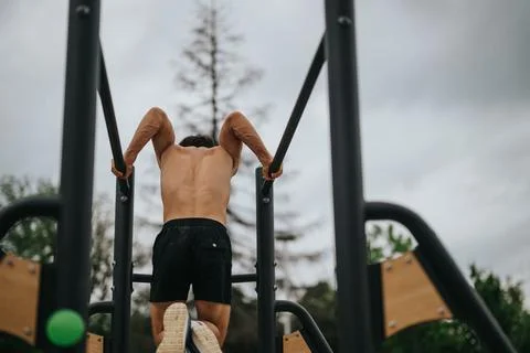 Athletic man exercising on outdoor parallel bars in a park Stock Photos