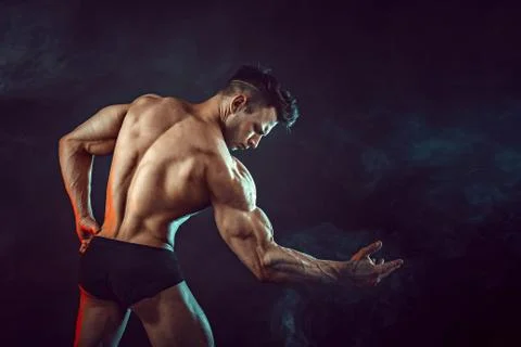 Athletic man flexing muscles in studio on dark background with smoke. Strong Stock Photos