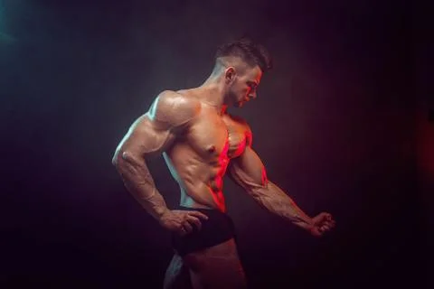 Athletic man flexing muscles in studio on dark background with smoke. Strong Stock Photos