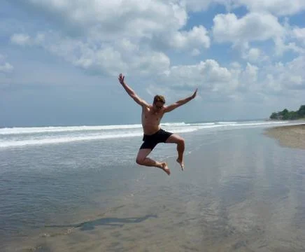 Athletic man jumping into the air on beach, Bali, Indonesia Stock Photos