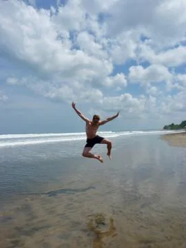 Athletic man jumping into the air on beach, Bali, Indonesia Stock Photos