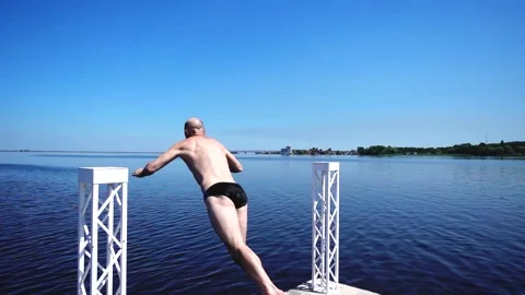 Athletic Man Jumping and Diving into a Calm Blue Lake from a Pier on a Summer Stock Footage 334595132