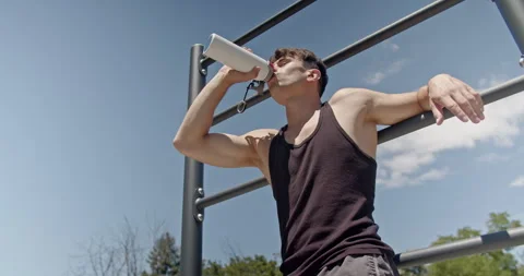 Athletic man leaning on parallel bars and drinking water while resting during Video stock 280435980