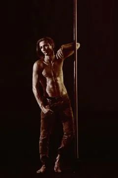 Athletic man make acrobatic elements on pylon. Strong dancer workout on pole Stock Photos