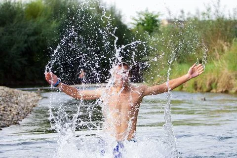 An athletic man makes splashes with his hands on the river. Stock Photos