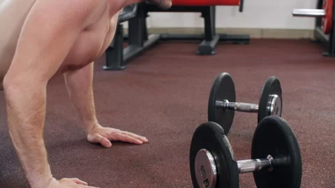 Athletic man is making push-ups on floor in gym near the dumbbells, side view. Stock Footage 231336748
