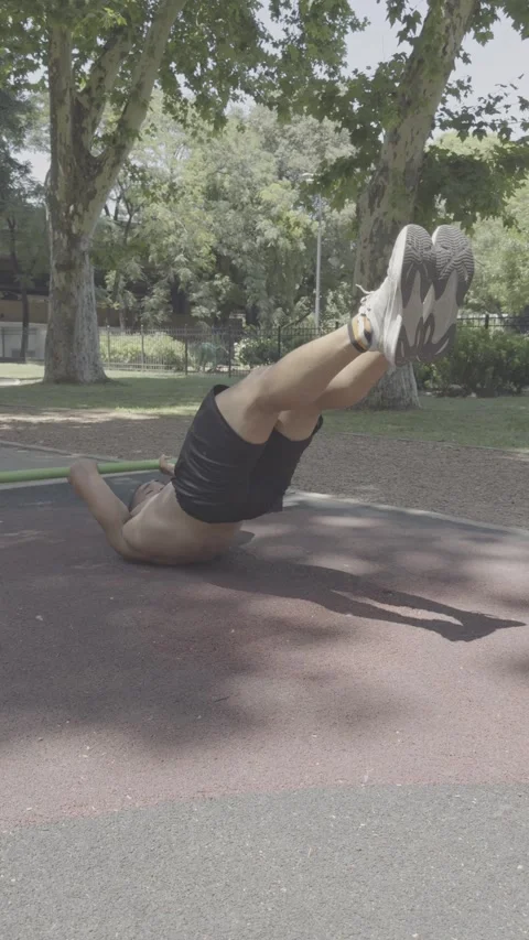 Athletic man performing abdominal exercises on a low bar in a park. Video stock 326683663