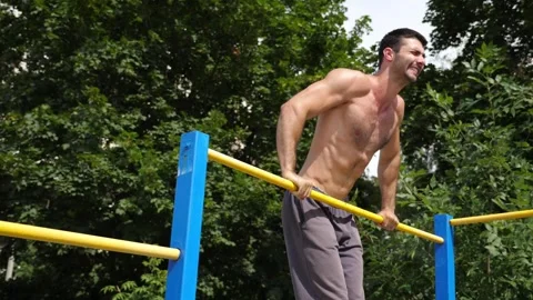 Athletic man performing dynamic workout routine on parallel bars, showcasing 库存影片 329757461