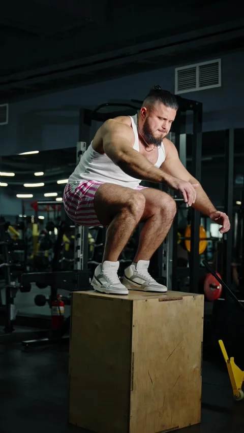 Athletic man performing explosive box jump exercise onto a wooden plyometric box Video stock 329557592