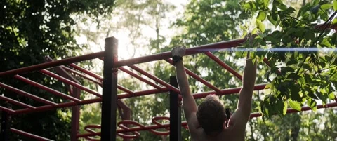 Athletic man performing pull-ups on outdoor workout bars in forest Stock Footage 323934189