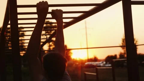 Athletic man performing pull ups on monkey bars at sunset outdoor fitness. Stock Footage 334718218