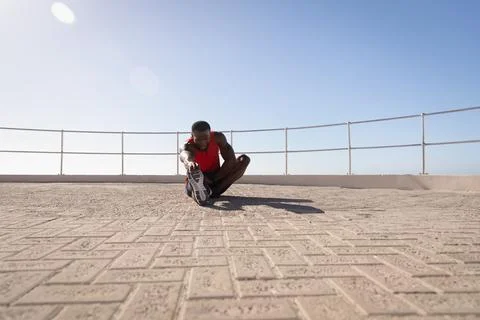 Athletic man performing seated hamstring stretch on seaside promenade with brick 写真素材