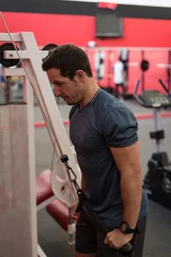 Athletic man performing tricep pushdown on cable pulley inside gym, with red and Foto stock